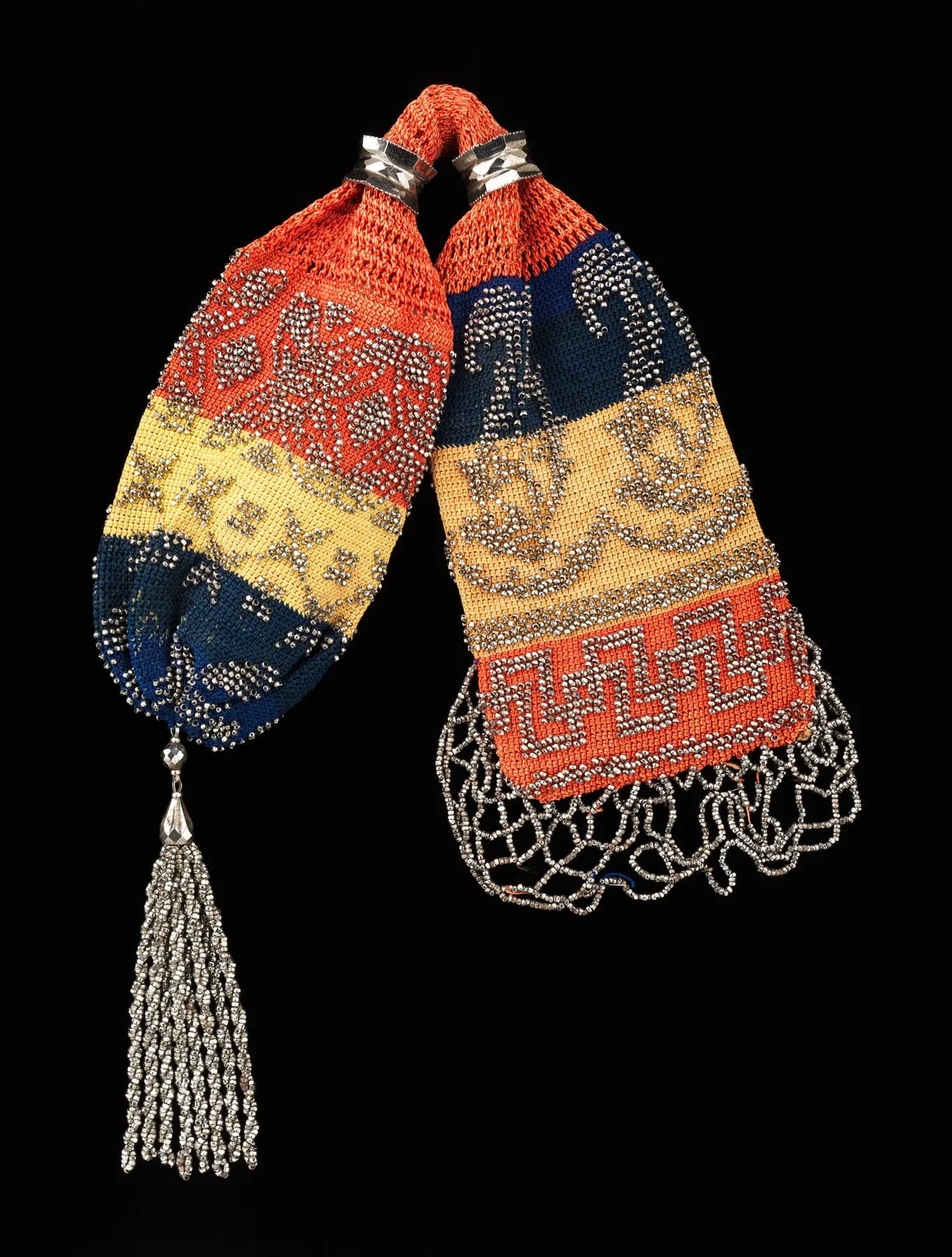 A long crocheted miser's purse in coral, gold and navy with a silver tassel, on black.